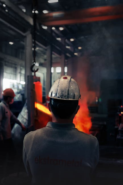 Back view of a worker in a helmet observing molten metal in an industrial setting with safety gear and smoke.